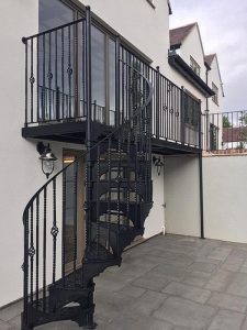 Full view of cast iron spiral leading to long balcony with basket and double twist balusters
